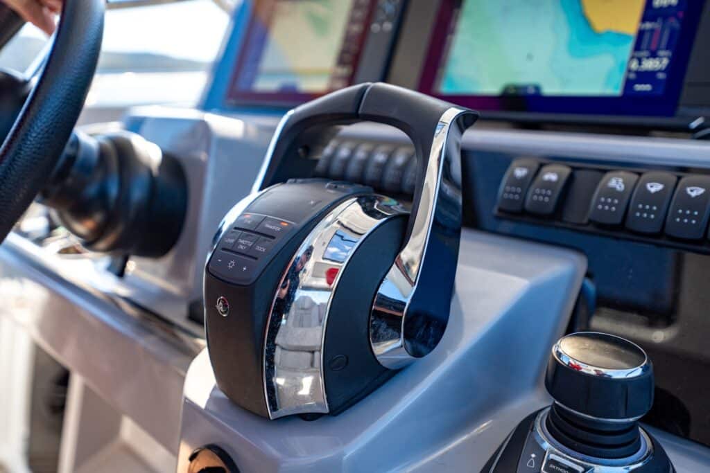 Close-up of a boat throttle control lever and joystick on a helm console, with navigation screens in the background.